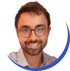 Profile photo of a smiling man with a beard and glasses, wearing a light blue shirt, set against a plain background, framed in a blue circle.