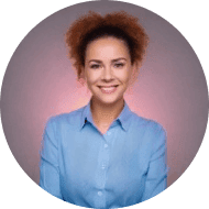 A woman with curly hair wearing a light blue shirt smiles at the camera with a neutral background.